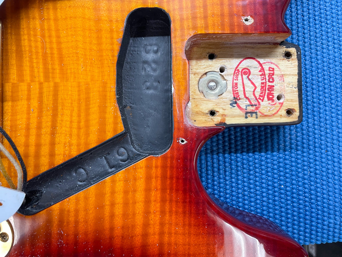 Close-up of the guitar's flame top body, showing the neck pocket with a red "John Cruz" stamp and the pickup cavity with "B23" and "C.19" markings.