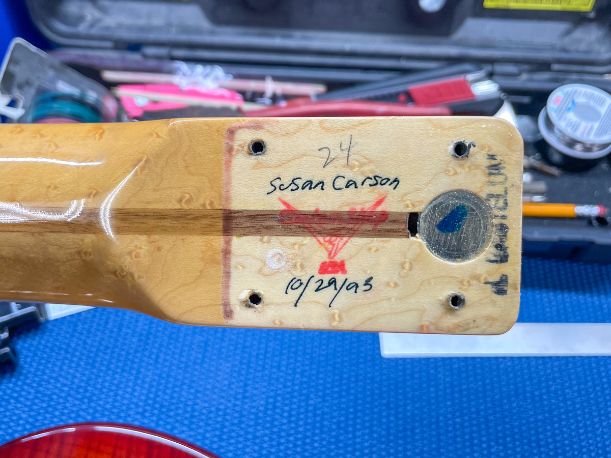 The guitar neck heel shows a light wood finish with visible grain, a red stamp, and handwritten black markings.