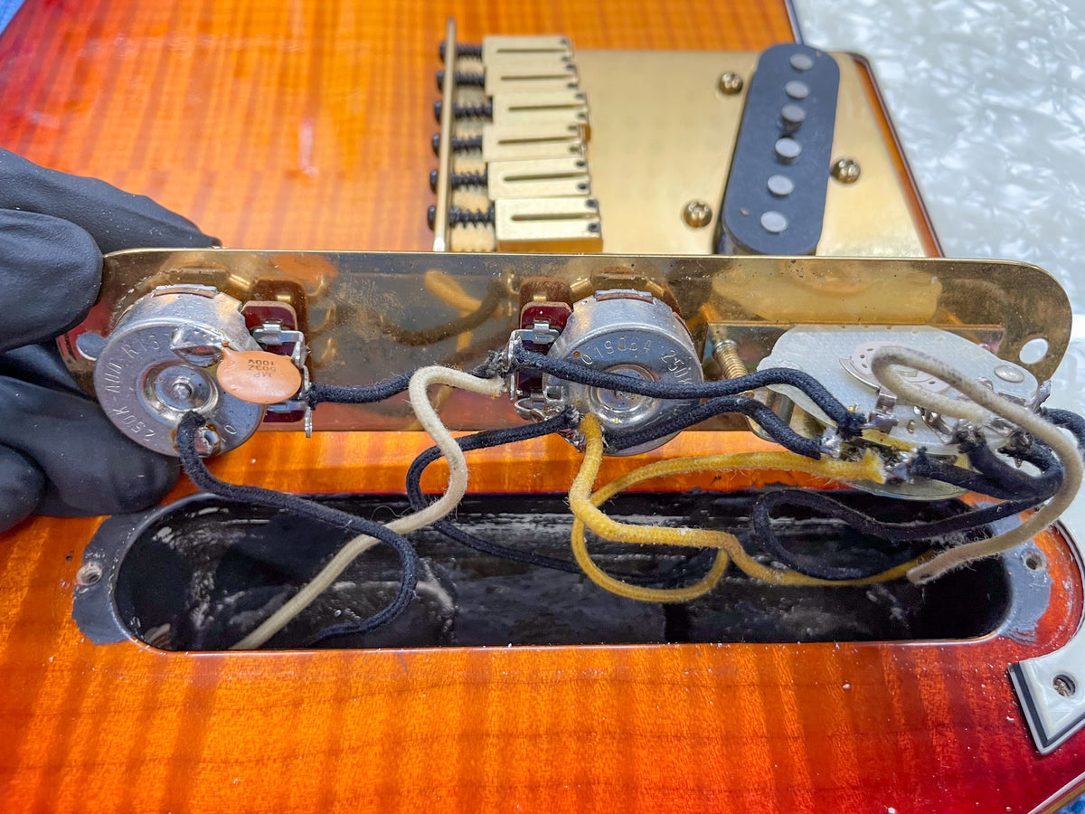 Close-up of the guitar's control cavity, revealing gold-plated hardware, three potentiometers, a capacitor, and wiring.