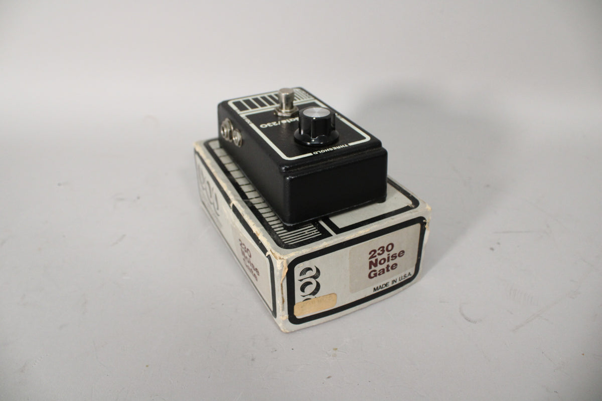 Black pedal with a silver footswitch and black knob, resting on its worn white box, viewed from the front-right.