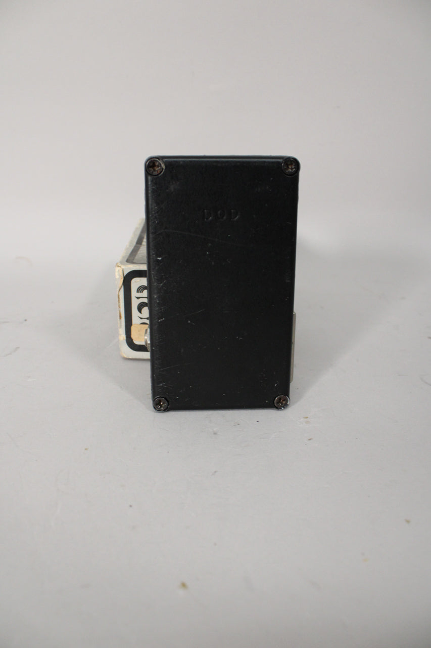 The black pedal is seen from the back, showing four screws and light wear on its matte finish, with a box partially visible left.