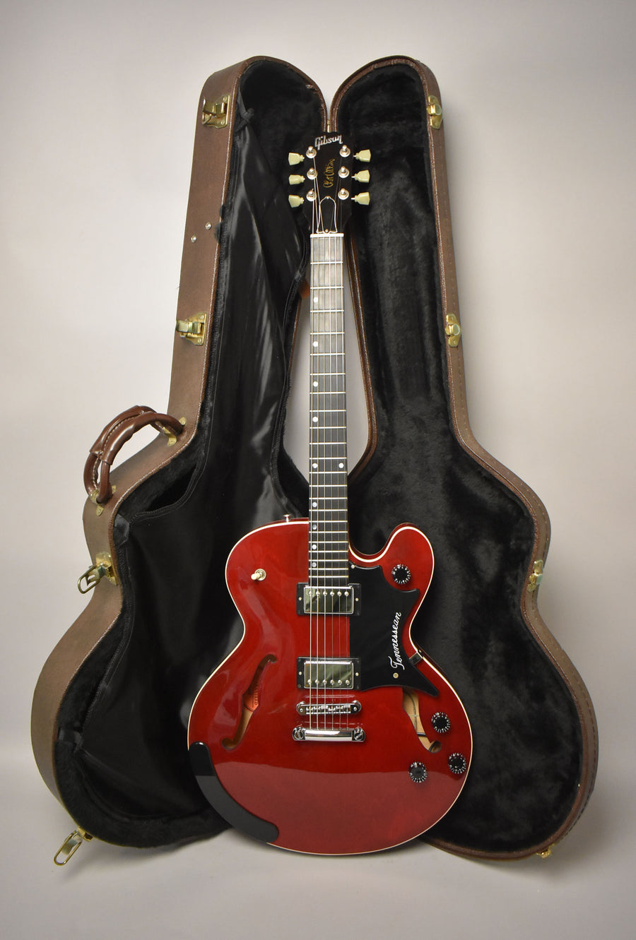Full-length view of a glossy cherry red semi-hollowbody electric guitar with chrome hardware, standing in its open brown hardshell case.