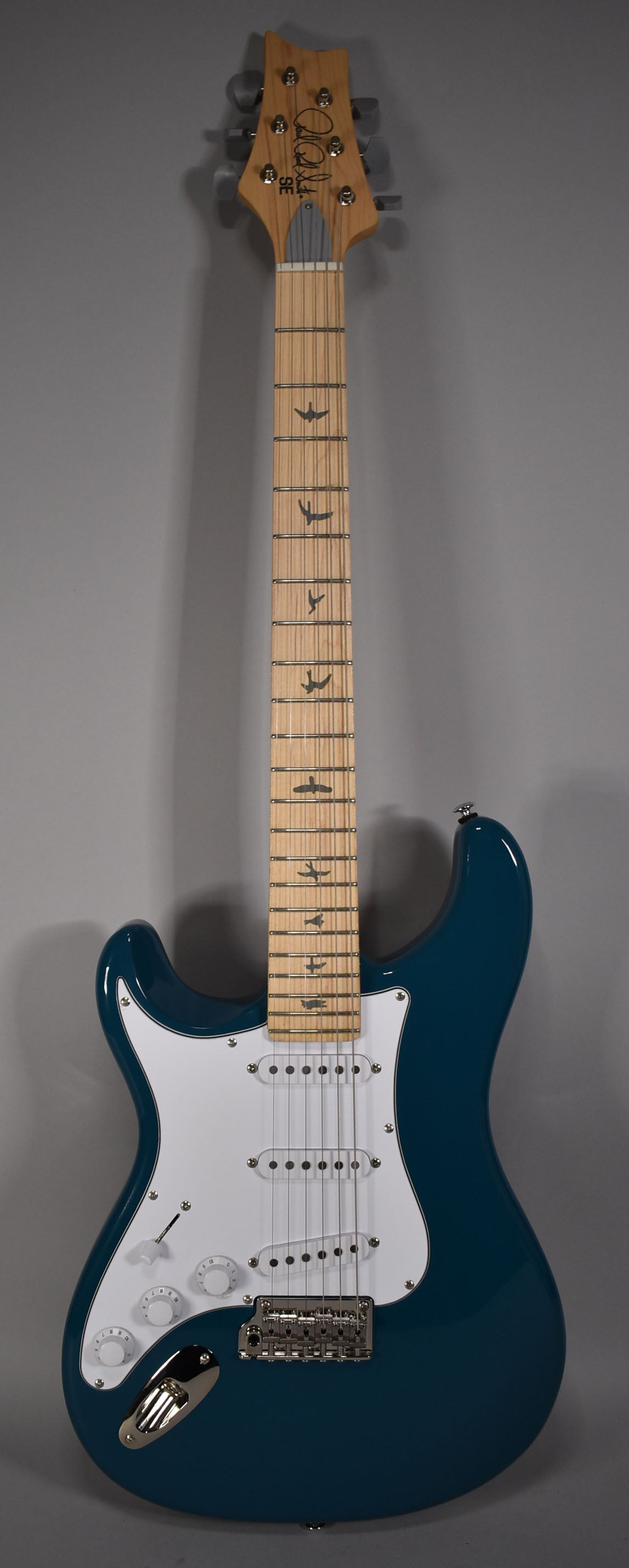 Full-length view of a glossy blue electric guitar with a white pickguard, three single-coil pickups, and a maple fretboard with bird inlays.