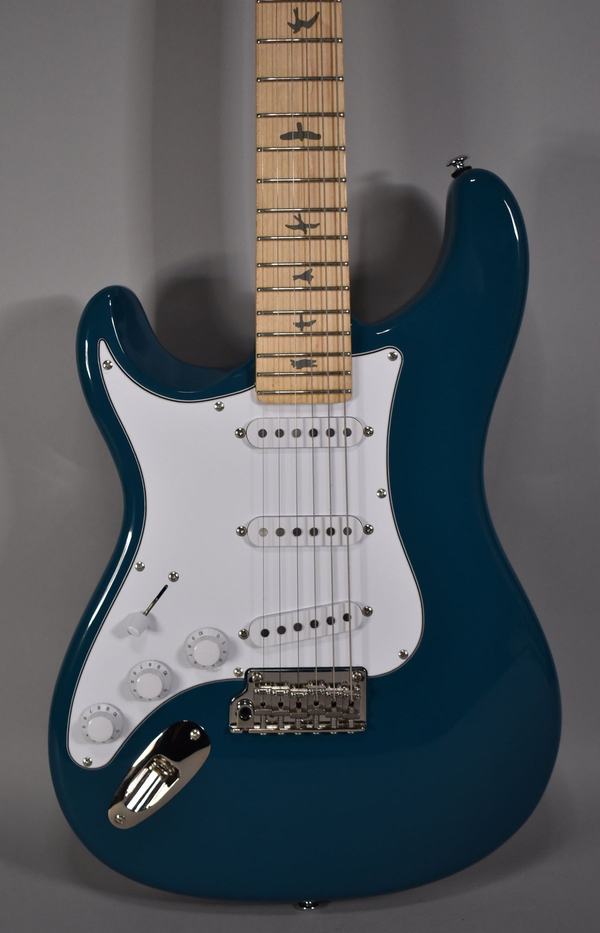 Full-frame view of a glossy blue electric guitar with a white pickguard, three single-coil pickups, and bird inlays on the maple fretboard.