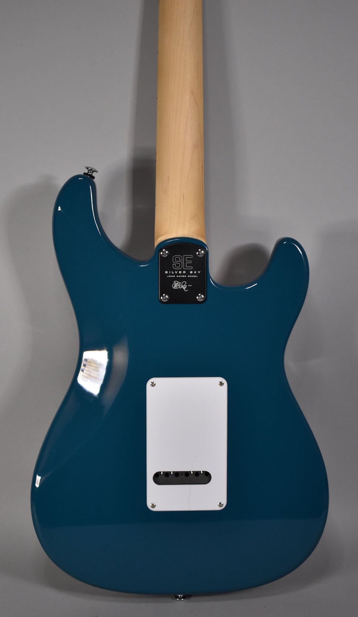 The back of a glossy blue guitar, with a light wood neck, and a white rectangular tremolo cover.
