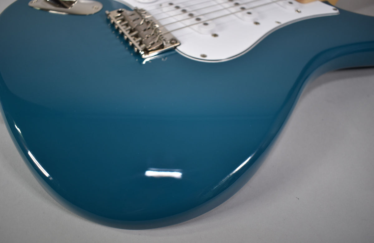 Close-up of the guitar's glossy blue body, showing the chrome tremolo bridge, white pickguard, and a hint of the fretboard.
