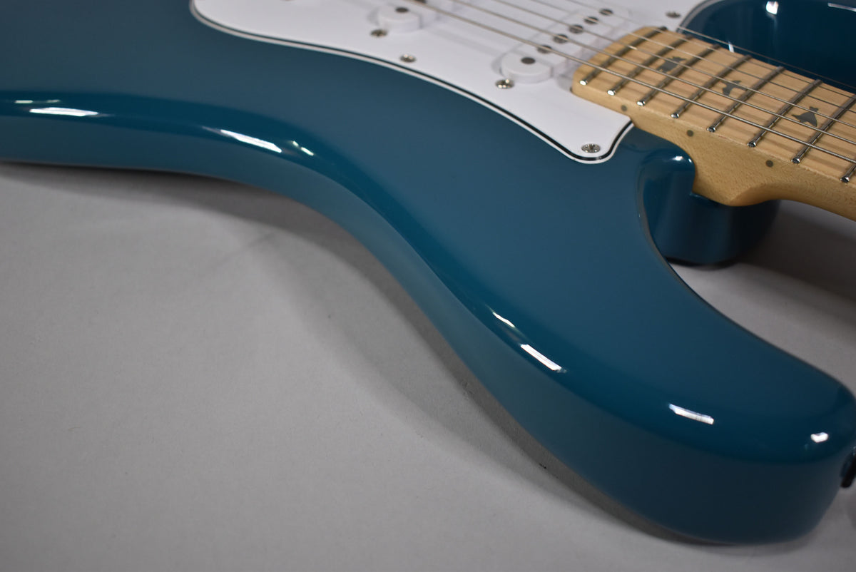 Close-up of the guitar's glossy blue lower bout and cutaway, with a white pickguard and maple fretboard visible at the top right.