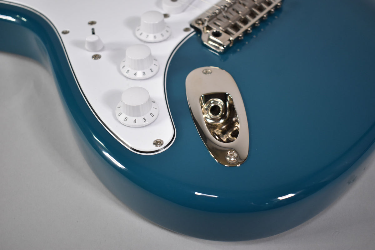 Close-up of the glossy blue body and white pickguard, showing three white control knobs, a switch, and a chrome output jack.
