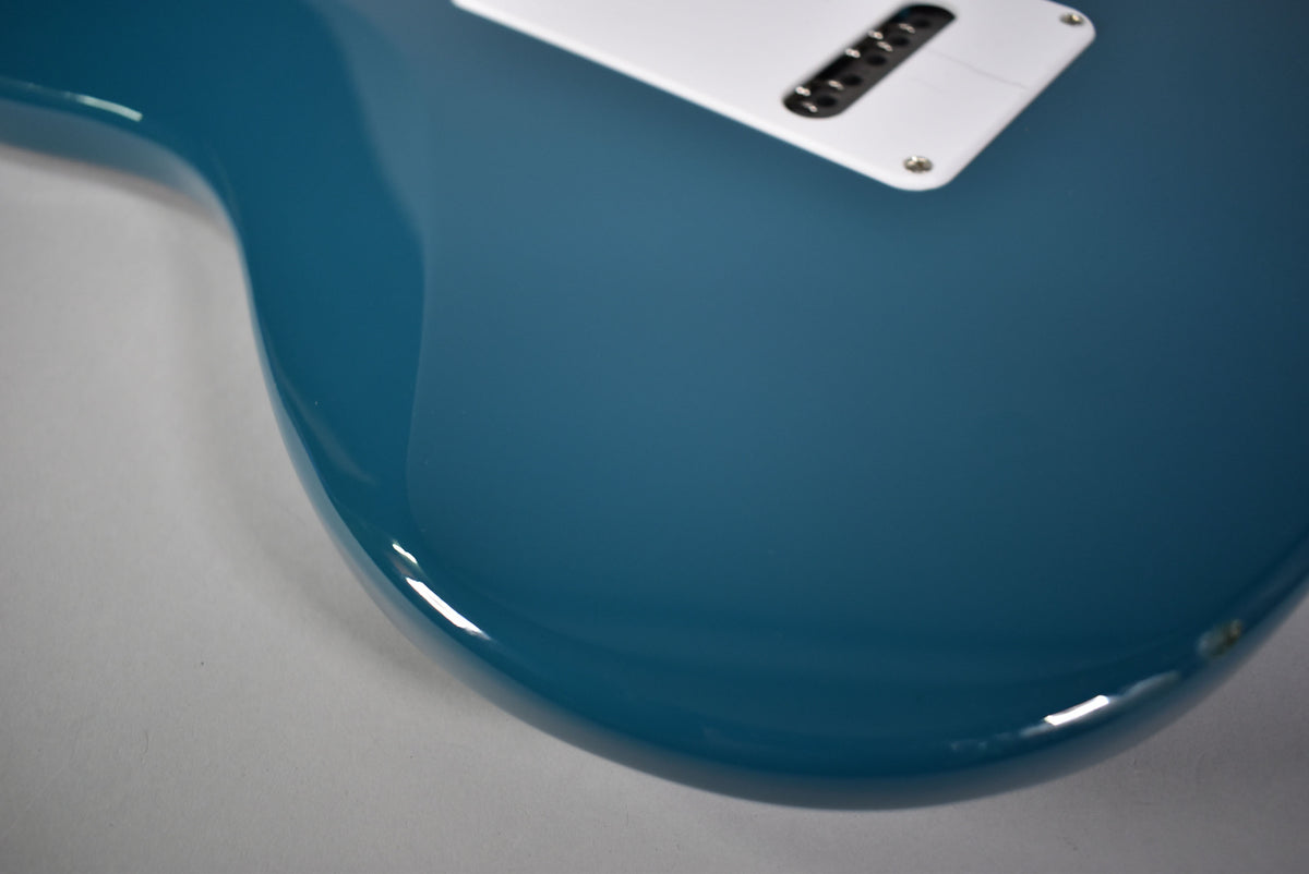Close-up of the guitar's lower body in glossy blue, showing the white tremolo cover and a small chip on the bottom edge.