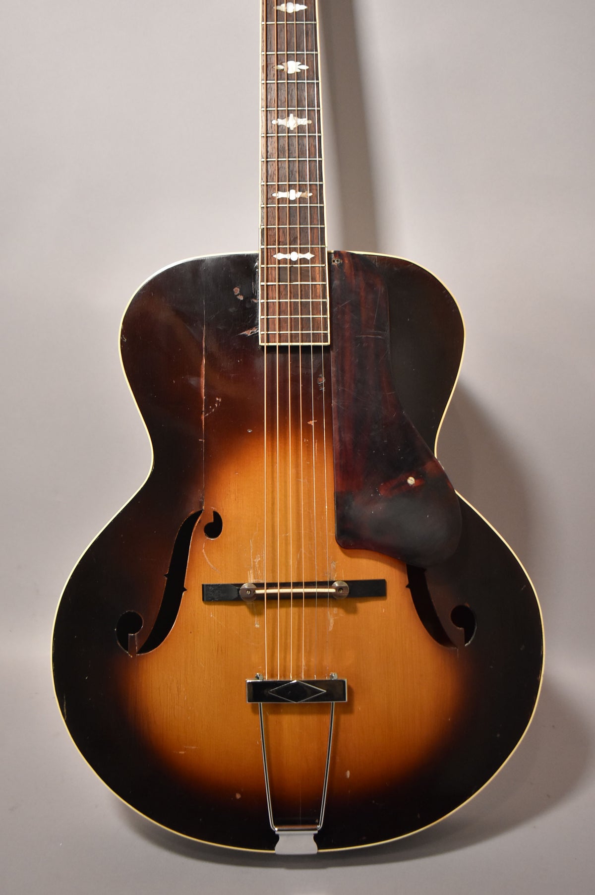 Full-frame view of the sunburst archtop's body and lower neck, showing f-holes, pickguard, and heavy finish wear.