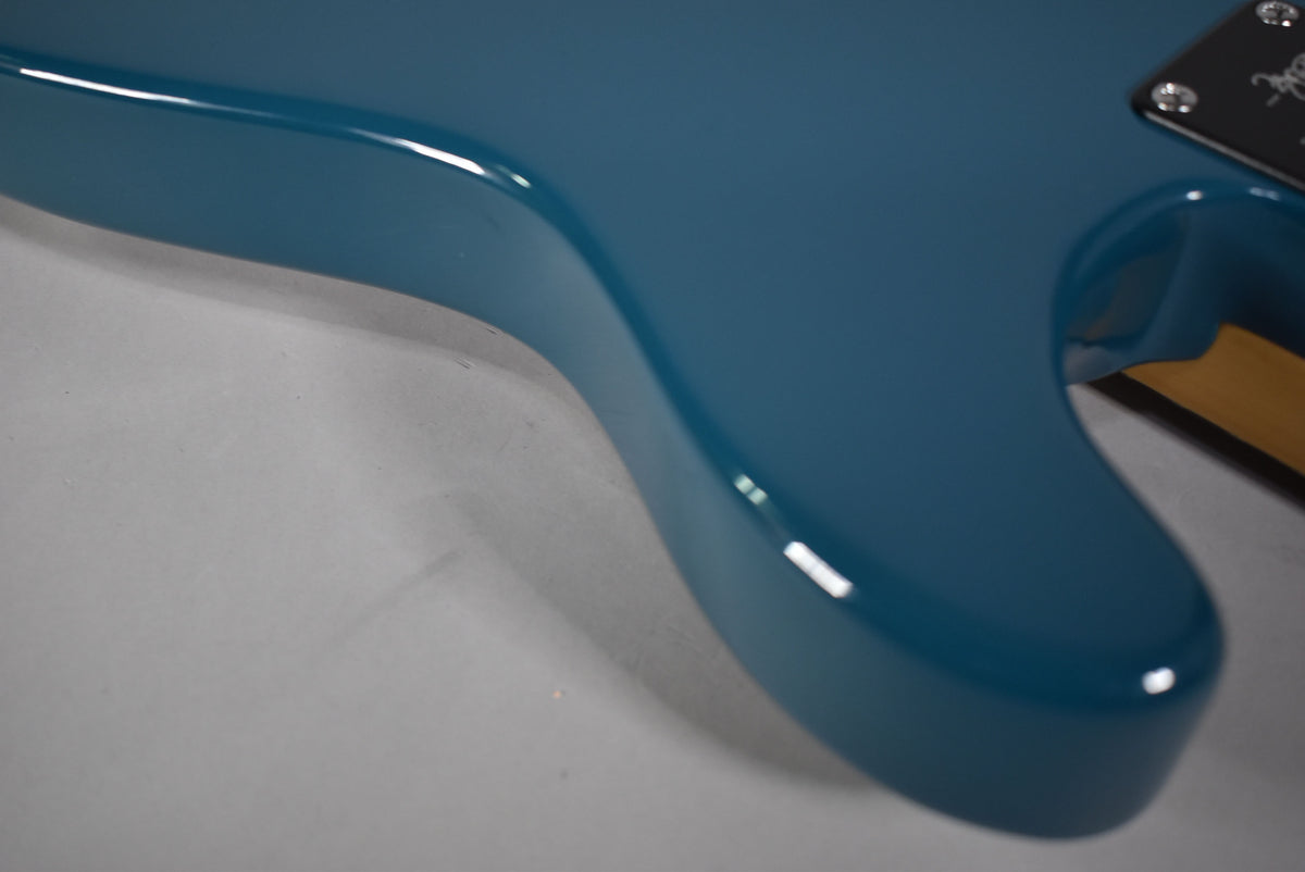 Close-up of the guitar's glossy blue body, showing the smooth curves of the lower bout and a glimpse of the neck joint.
