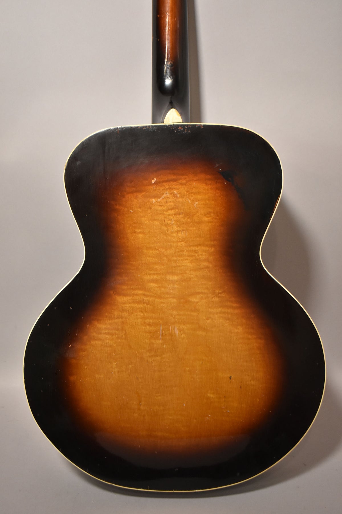 The guitar's sunburst back shows a dark brown edge fading to amber, with visible finish checking and wear, and a dark neck heel.