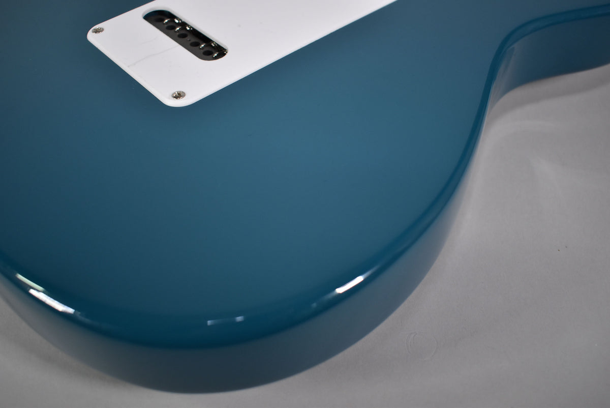 Close-up of the guitar's glossy Nylon Blue body, showing the white tremolo cover and string-through-body bridge from the back.