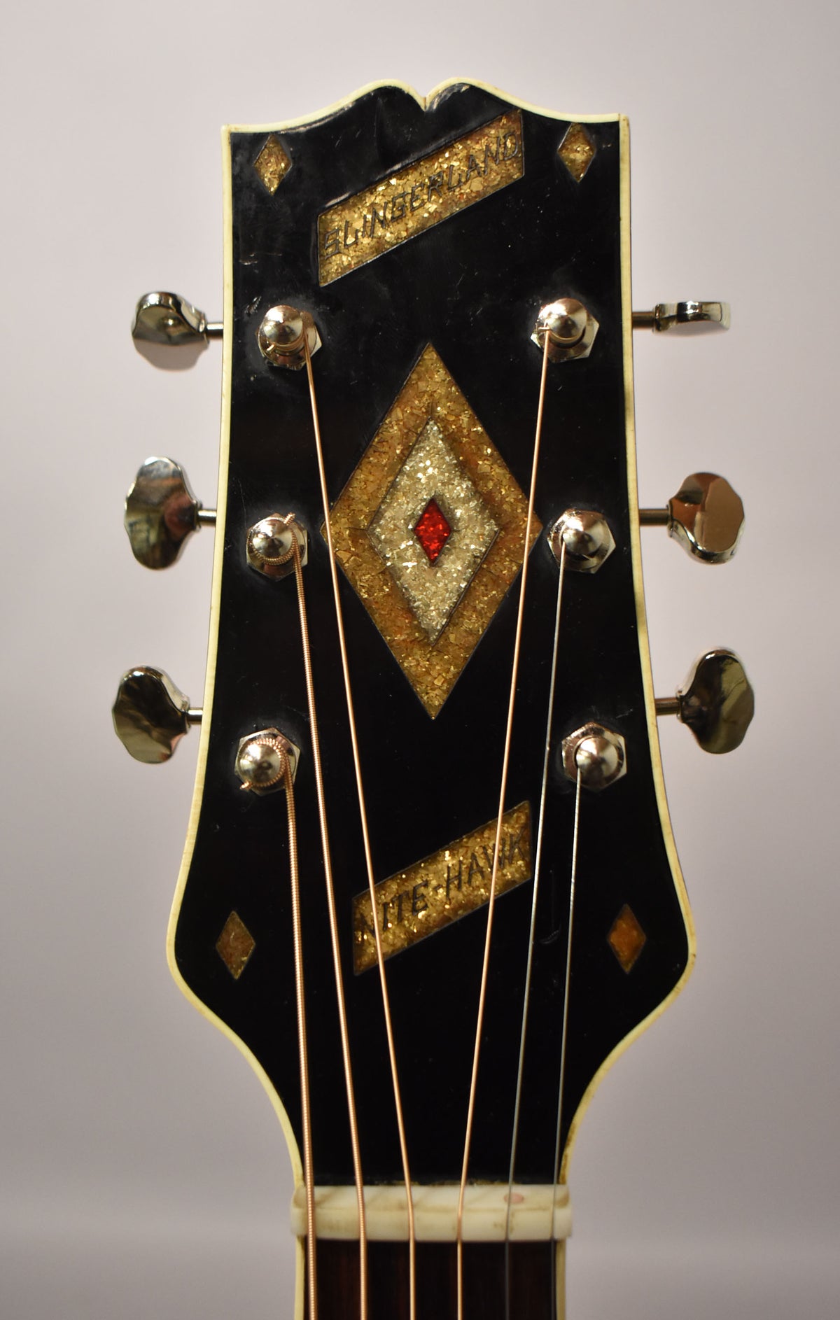 Close-up of the black headstock with gold glitter inlays, a red diamond, and six chrome tuners.