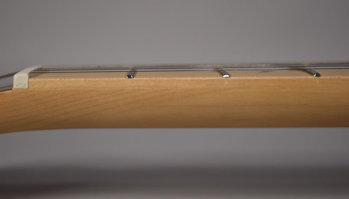 Close-up, side view of the guitar's light brown maple neck and fretboard, showing the white nut and first few frets.