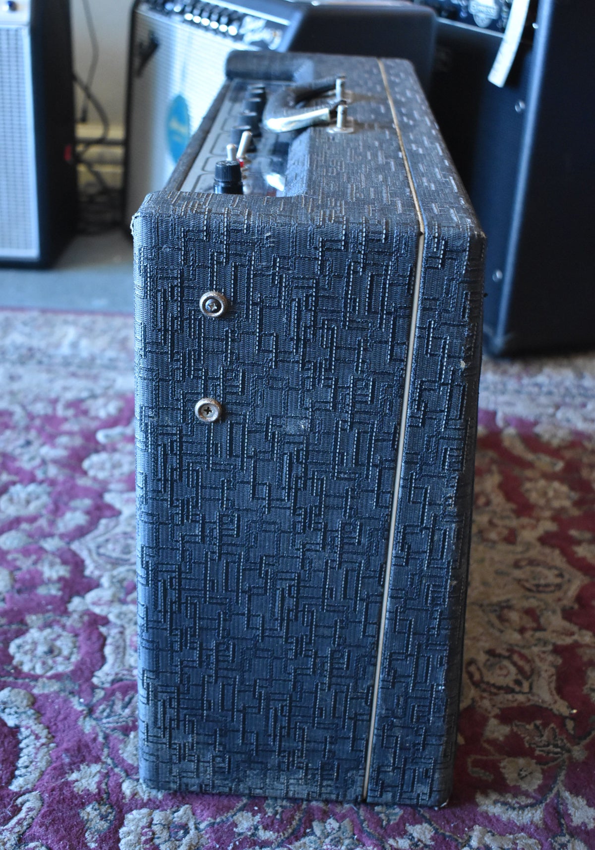 The amp's right side is visible, showing its dark blue textured tolex, two silver feet, and a thin cream piping strip.