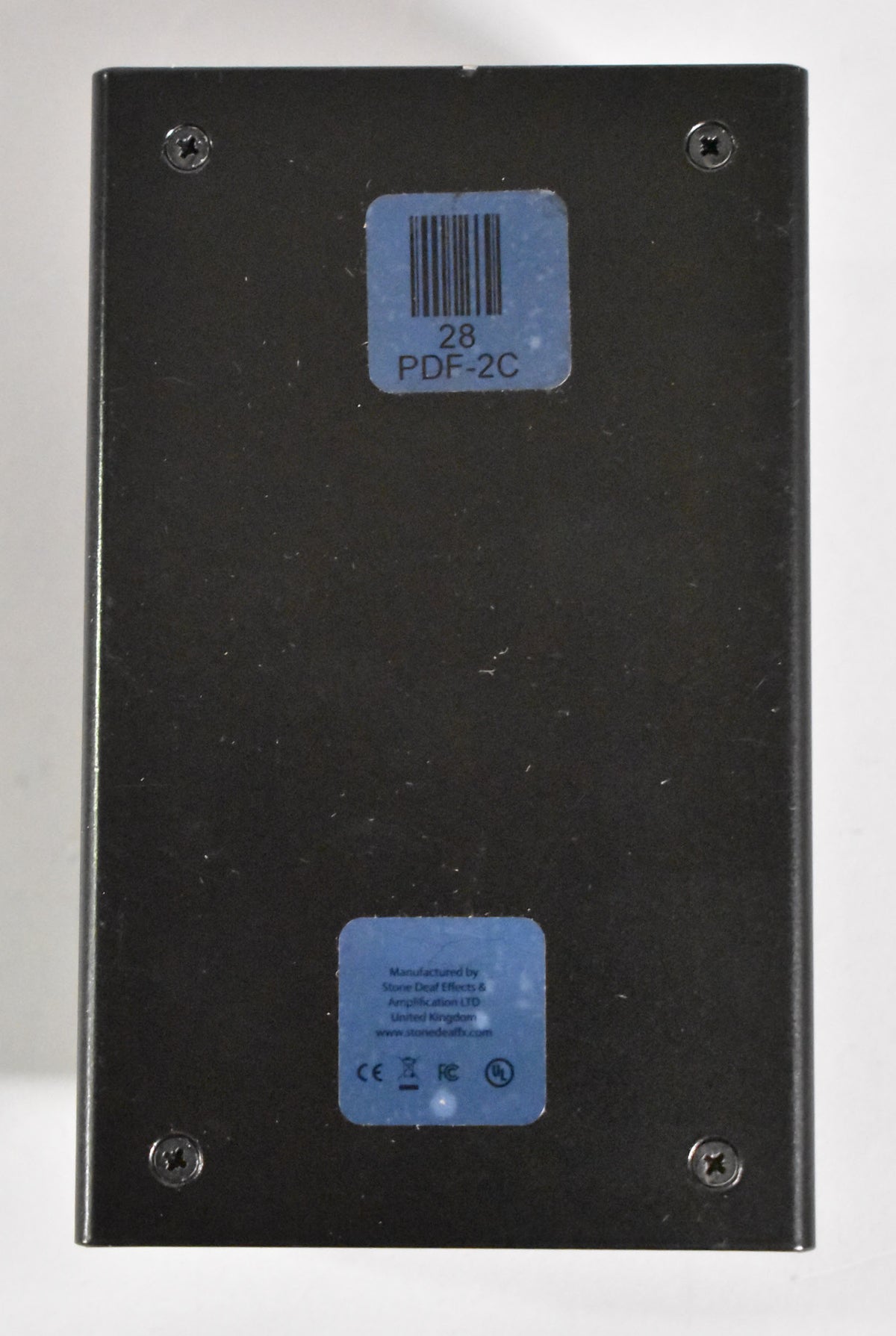 The pedal's black metal underside is visible, secured by four screws, with two blue product information stickers.