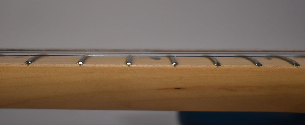 A close-up, side view of the guitar's maple fretboard, showing six silver frets and strings, with a slight dark smudge near the third fret.