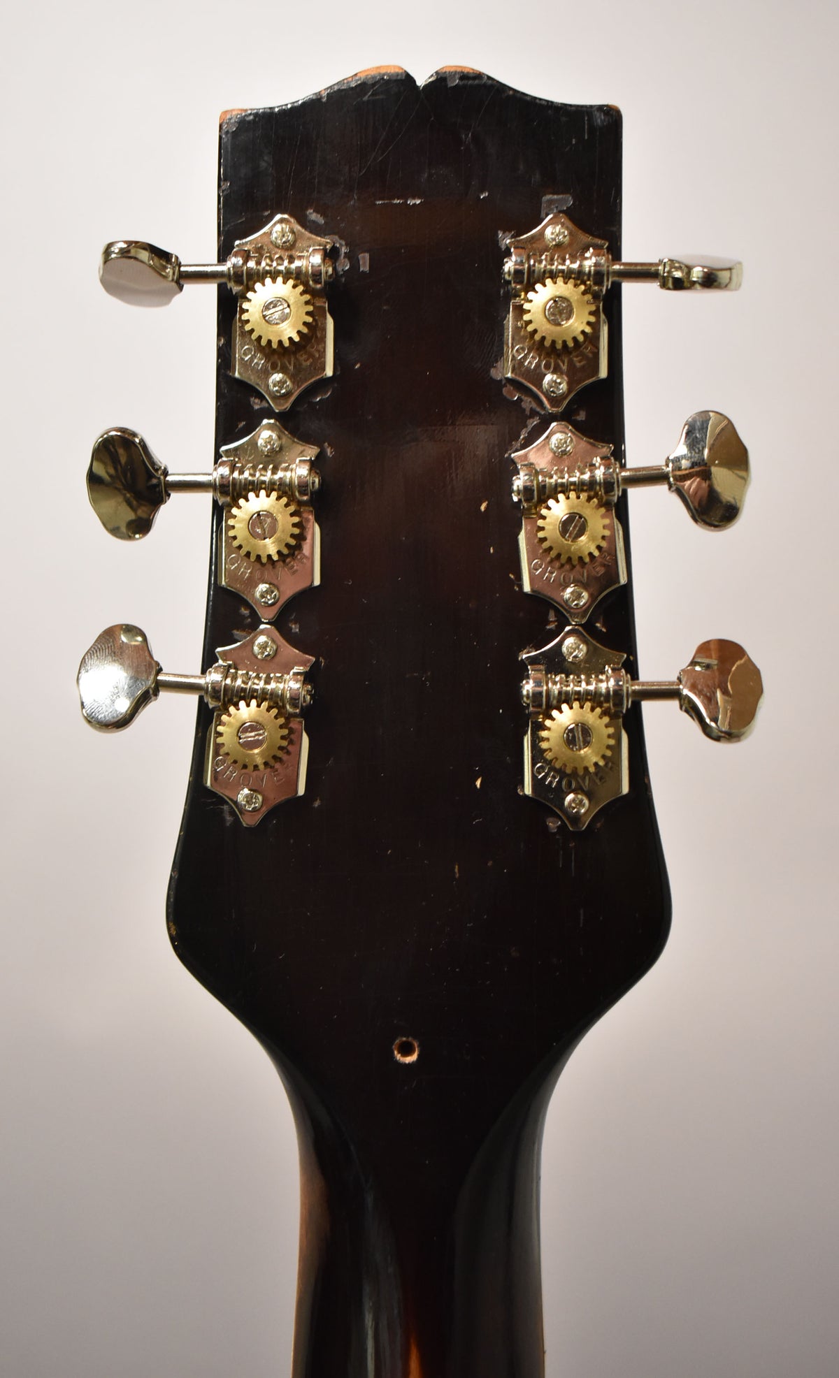 The dark brown headstock's rear shows six chrome tuners with brass gears, and wear along the top edge.