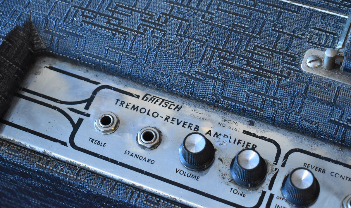 Close-up of the amp's worn silver control panel, showing two input jacks, Volume and Tone knobs, and blue patterned grille cloth.