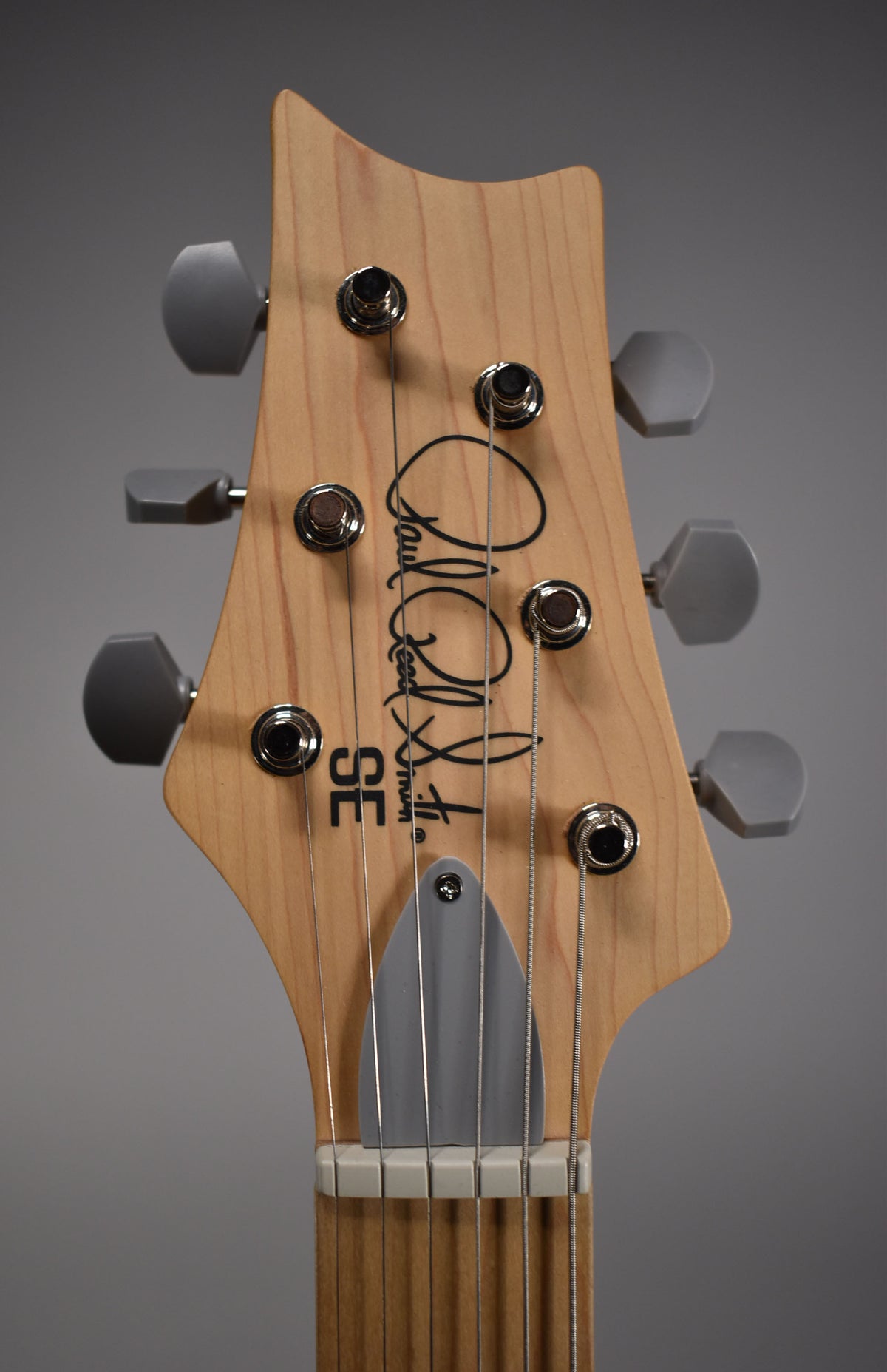 Close-up of the light wood headstock with six gray tuning pegs, a gray string tree, and a white nut.