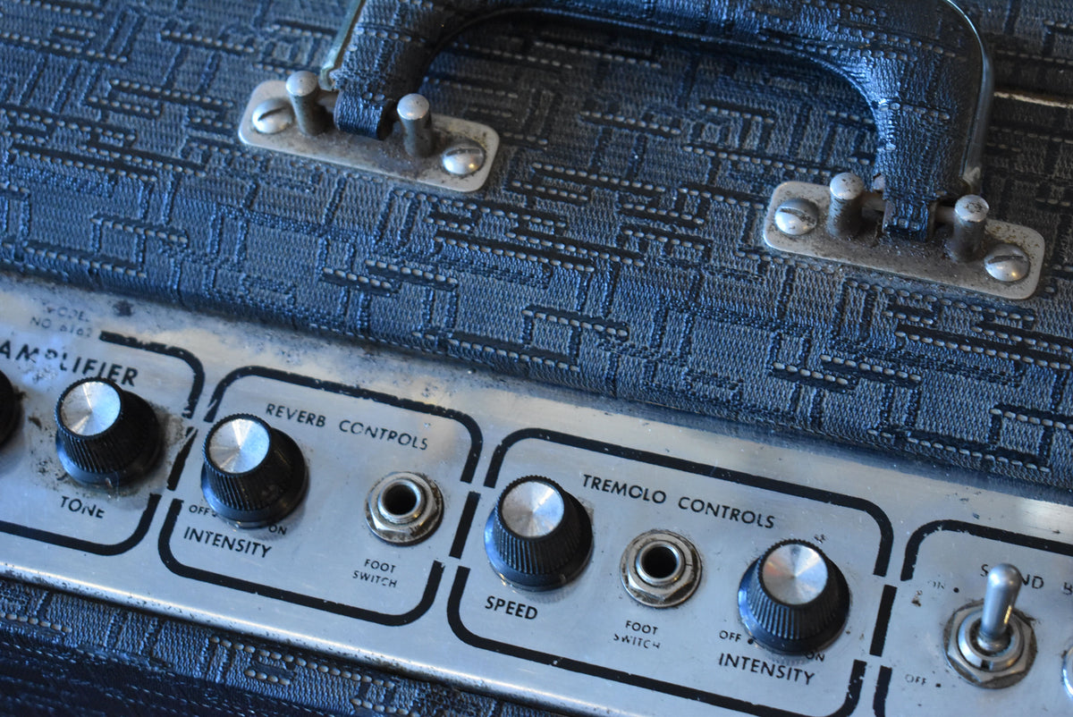 Close-up of the amp's top, showing the black textured handle, worn silver control panel with black knobs, and "Reverb" and "Tremolo" controls.