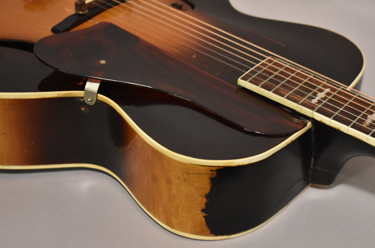 Close-up of the guitar's lower bout, showing the dark sunburst finish, cream binding, and a tortoiseshell pickguard with a metal bracket.