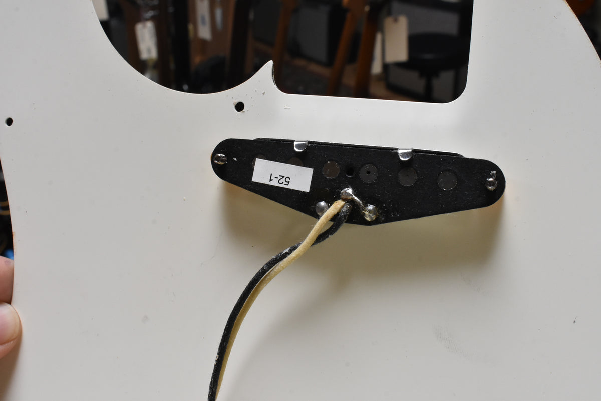 The underside of a white pickguard, revealing a black bridge pickup with a "52-1" sticker and braided wire.