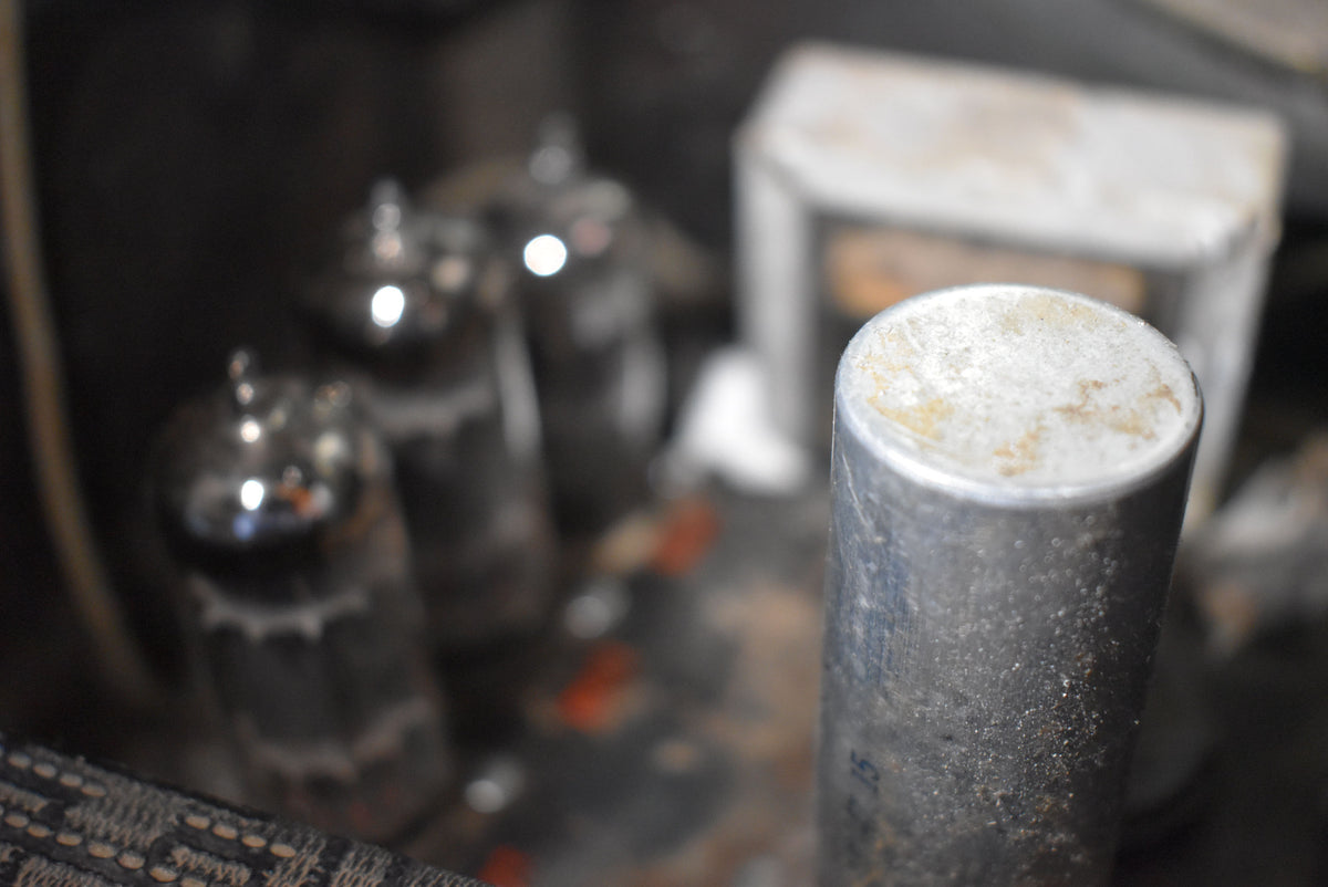 Close-up of the amp's internal components, showing several shiny vacuum tubes and a large, cylindrical, weathered silver capacitor.