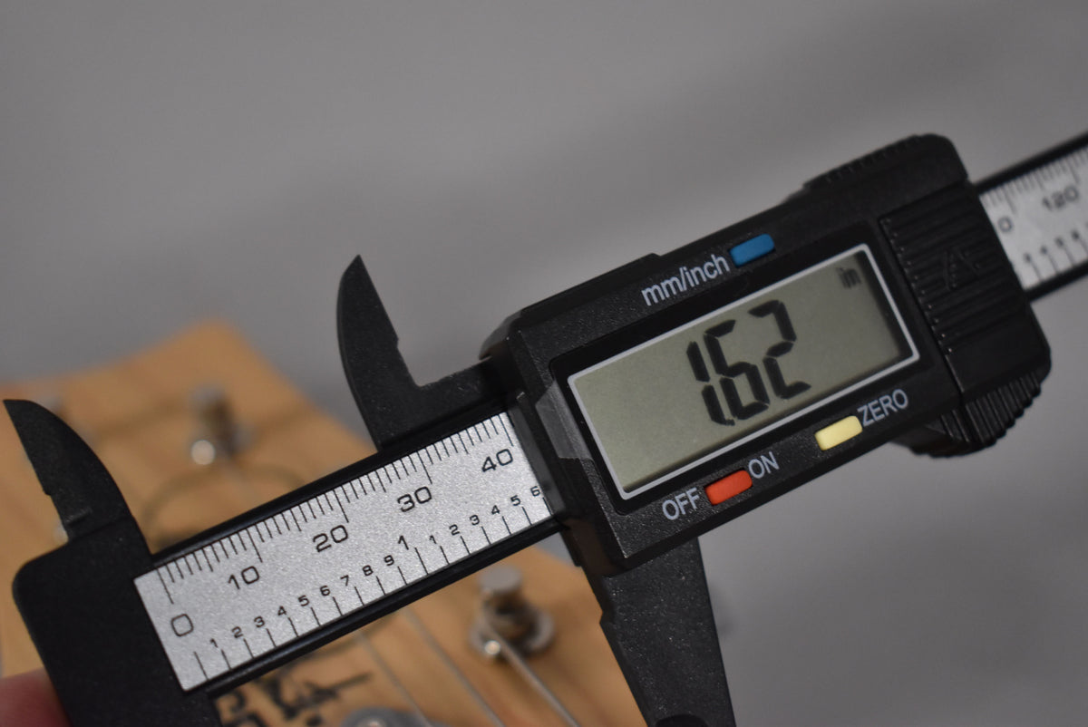 A digital caliper measures the guitar's nut width at 1.62 inches, with the headstock and tuning pegs visible in the background.