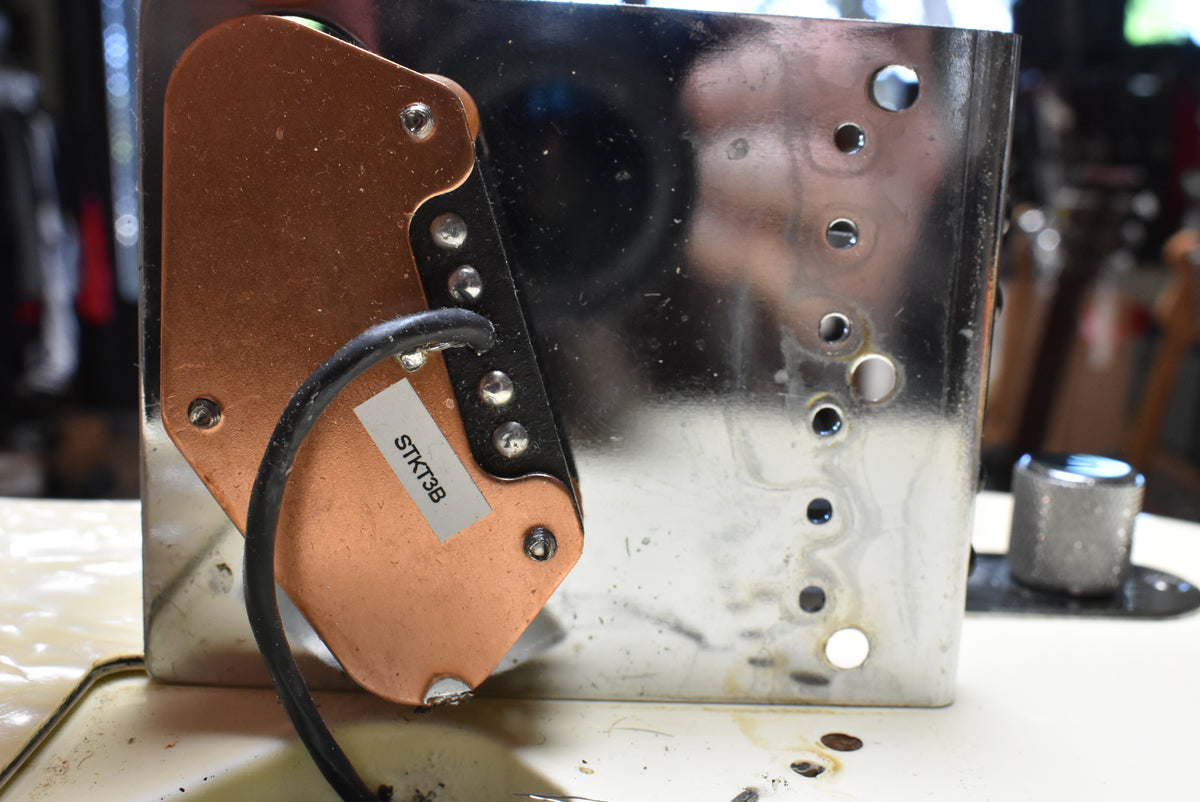 Close-up of the guitar's copper-colored bridge pickup with a "STKT3B" label, mounted on a worn chrome bridge plate with visible holes.
