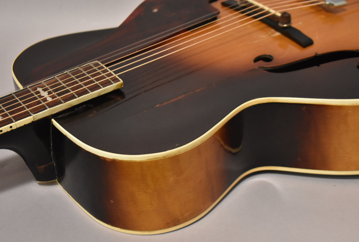 The sunburst archtop's lower bout and neck heel show a dark brown finish with light brown sides, cream binding, and finish checking.