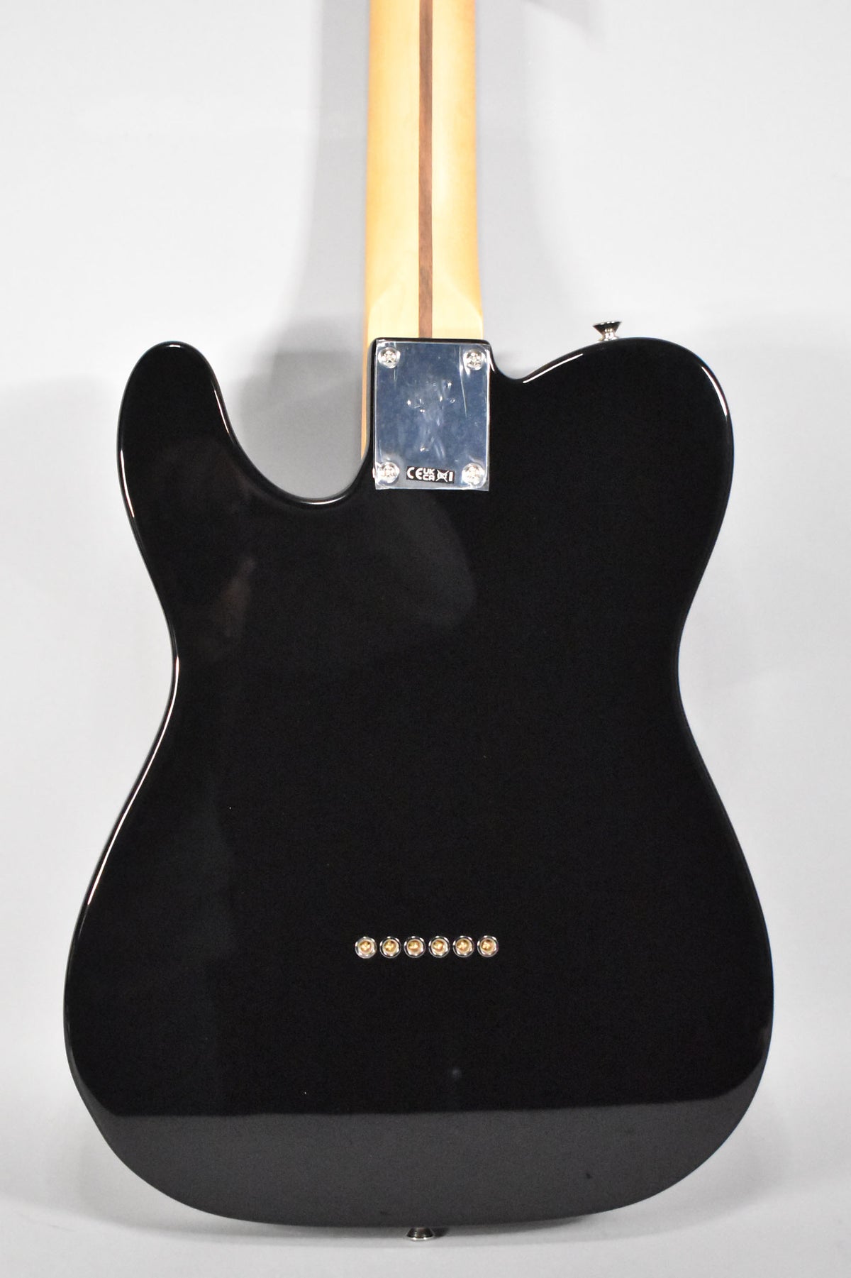 The back of a glossy black Telecaster, showing a light wood neck, chrome neck plate, and six gold string ferrules.