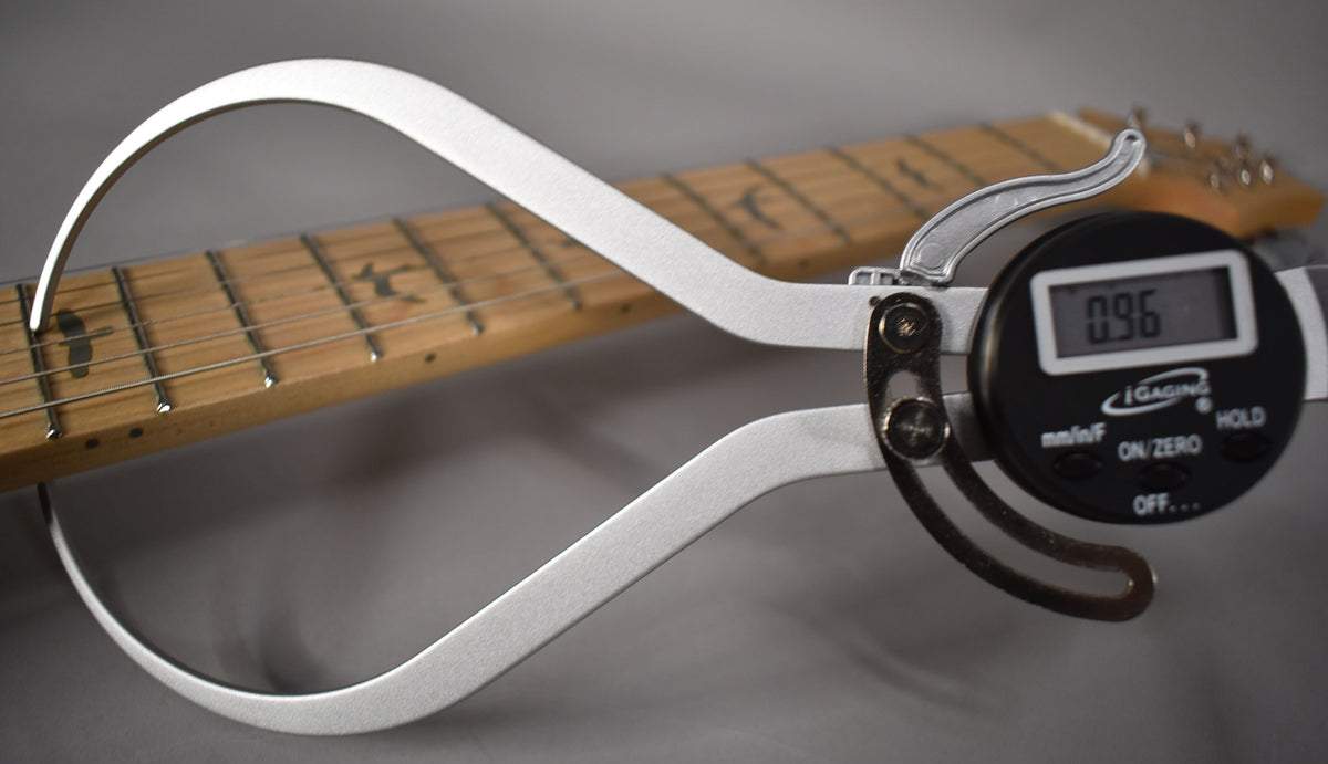 A digital caliper measures the string height at the 12th fret of the maple fretboard, showing 0.96mm.