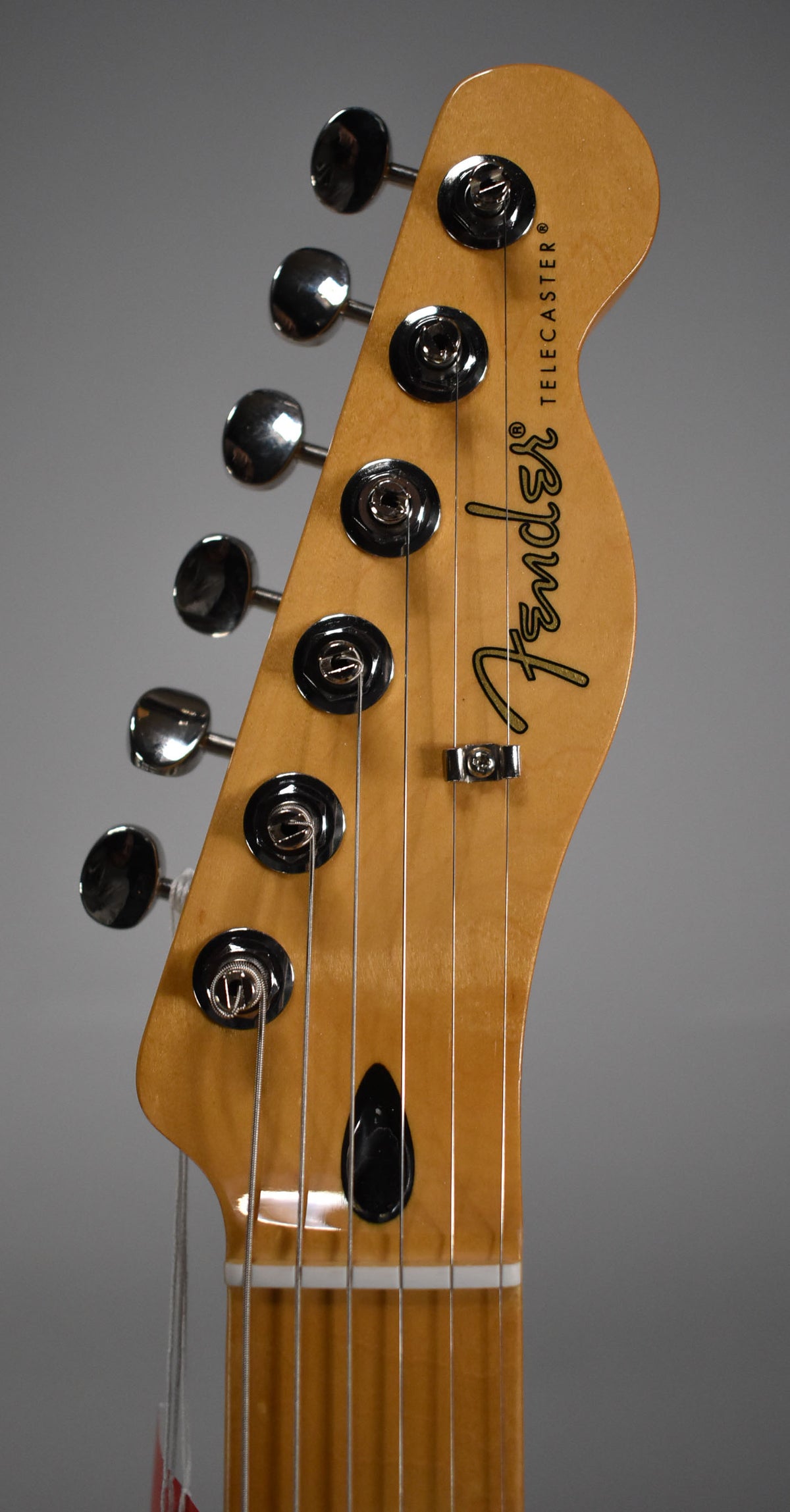 Close-up of the Telecaster's light wood headstock, angled left, showing six chrome tuners, a string tree, and the nut.