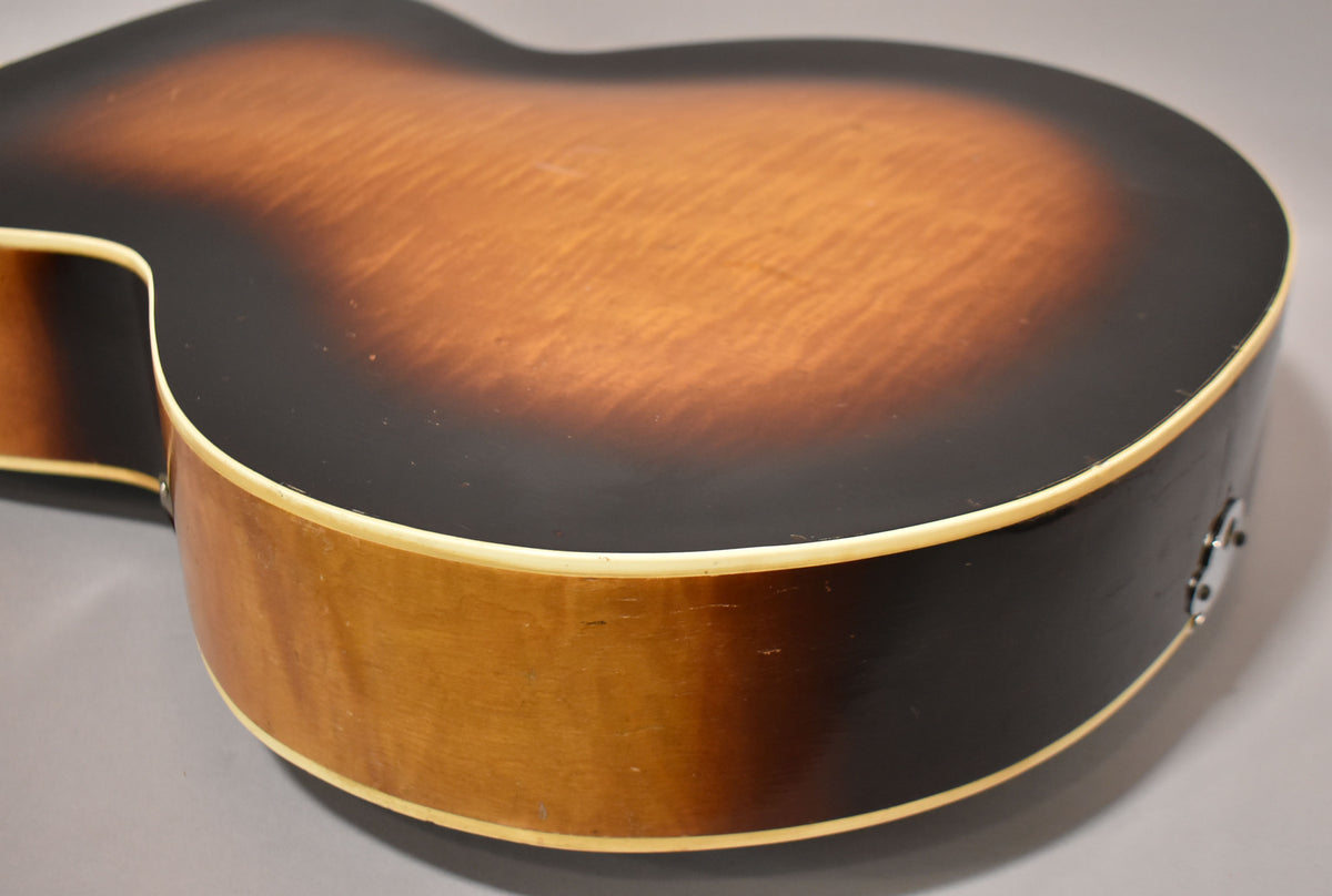 The guitar's sunburst back and side are visible, with light checking and wear, and a chrome endpin jack.