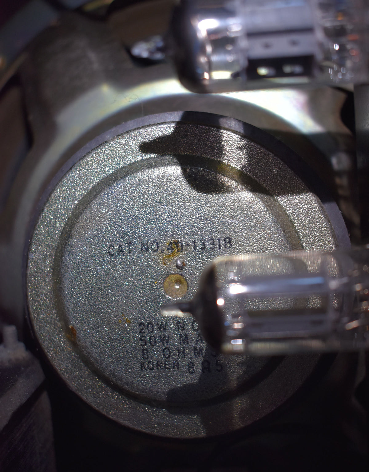 Close-up of the amplifier's internal speaker magnet, showing a speckled gray finish, some rust spots, and a vacuum tube in the foreground.