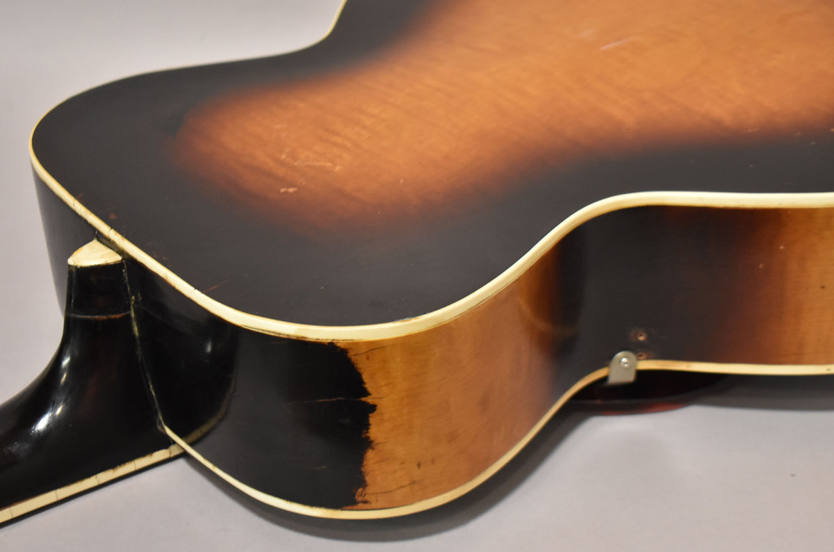 The guitar's sunburst finish shows heavy wear and checking on the lower bout and neck heel, with cream binding.
