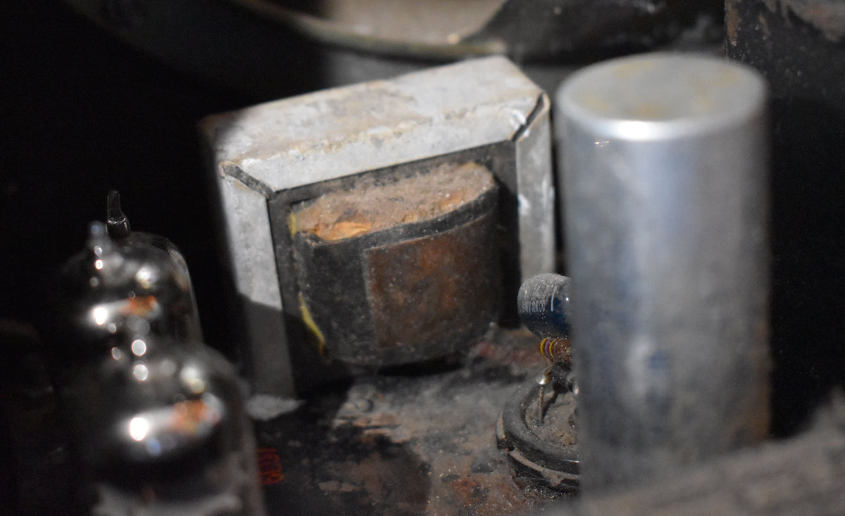 A close-up of the amplifier's internal components, showing a rusty transformer, a silver tube, and a smaller blue component with coiled wire.