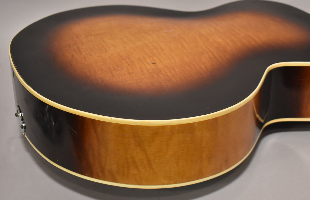 The guitar's lower bout and side are visible, showing a sunburst finish with wear, binding, and two strap buttons.