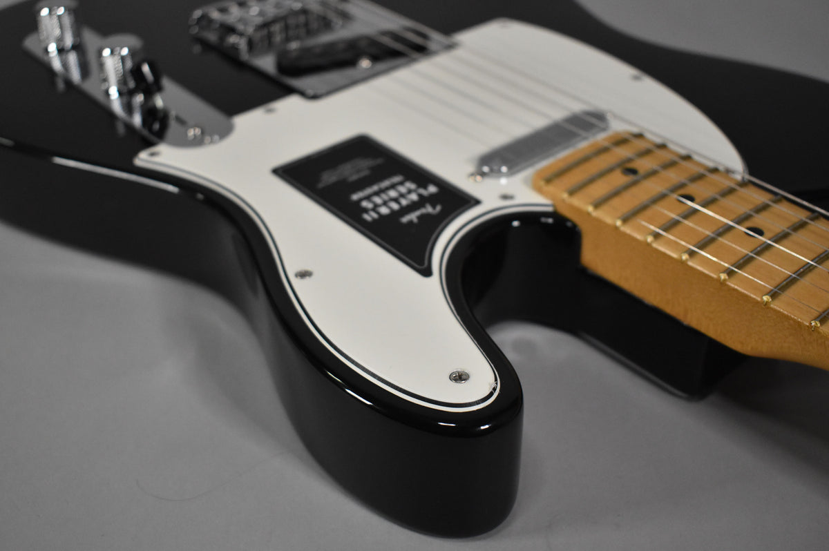 Black Telecaster body with a white pickguard and black trim, showing the lower bout and part of the maple fretboard.