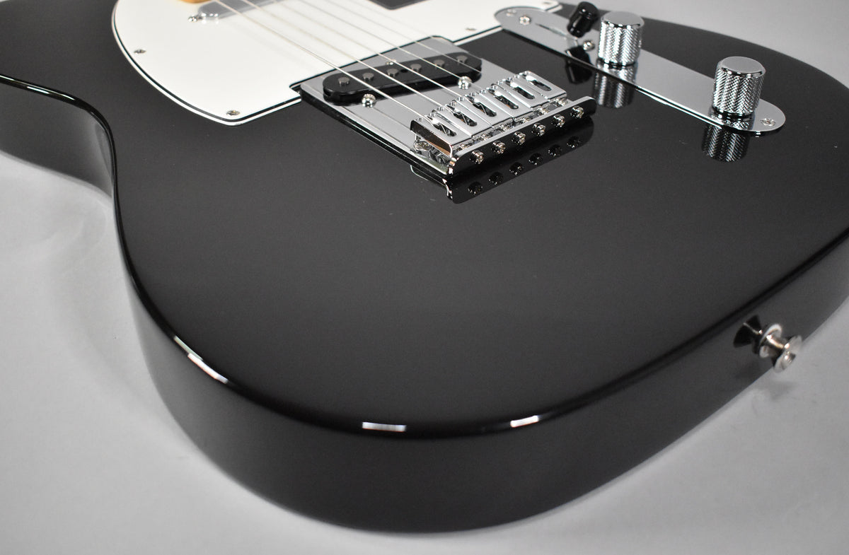 The black Telecaster body, with a white pickguard, chrome bridge, and knurled control knobs, is viewed from the lower bout.