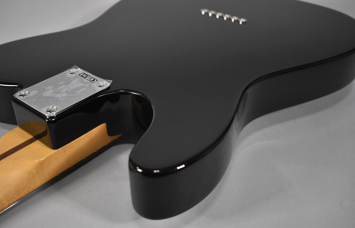 The black Telecaster body, with a glossy finish, is seen from the back, showing the neck plate and six string-through-body ferrules.