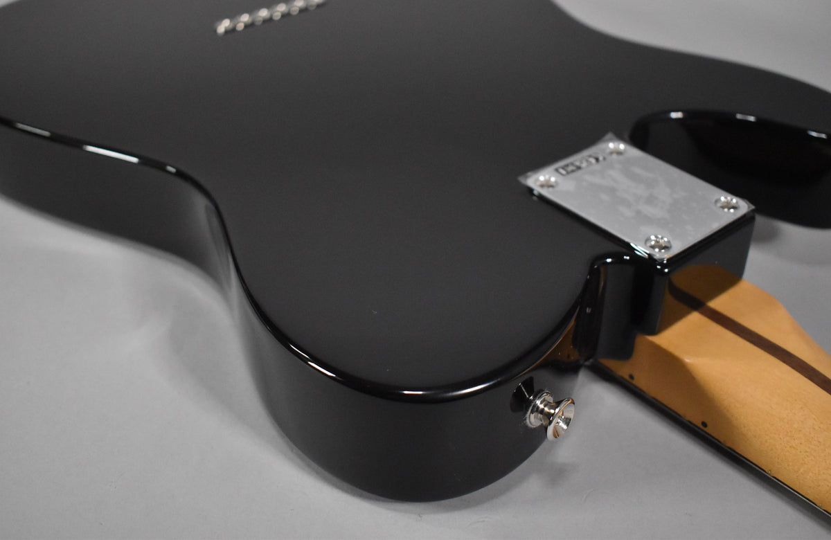The black Telecaster body, with a glossy finish, is seen from the back, showing the chrome neck plate and strap button.