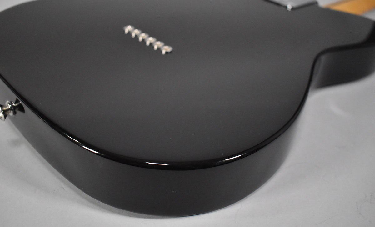 The guitar's lower bout is angled, showing the glossy black finish on the curved edge and the matte black top with six chrome string ferrules.