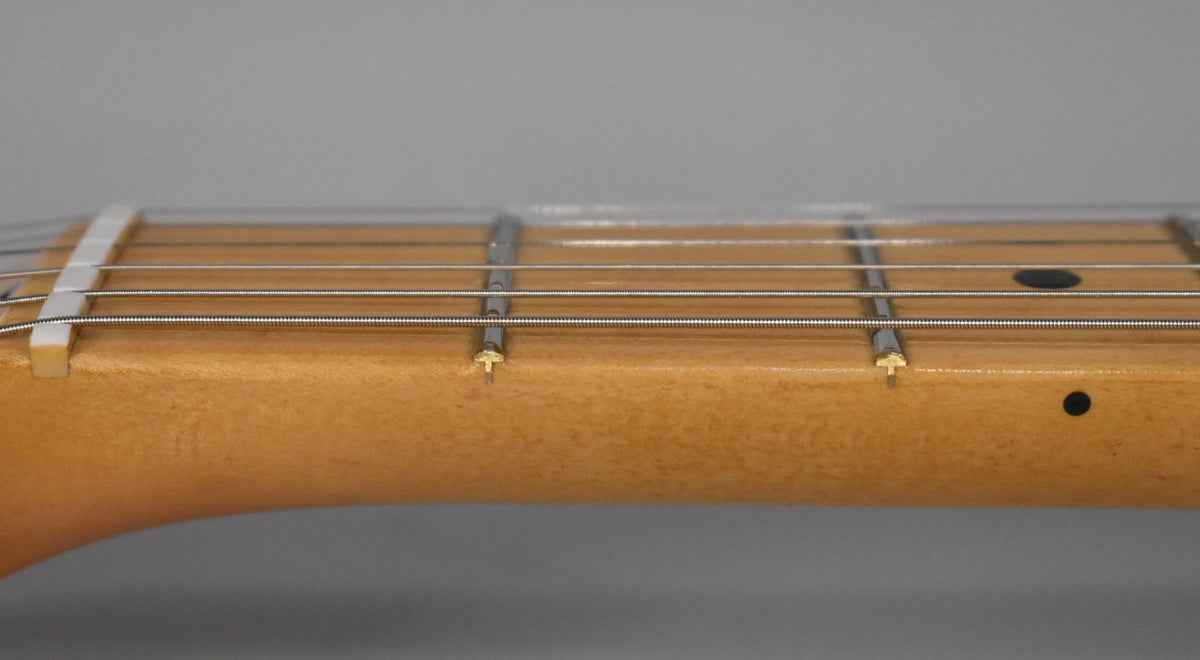 Close-up of the guitar's light-colored maple neck and fretboard, showing the nut, first few frets, and two black dot inlays.