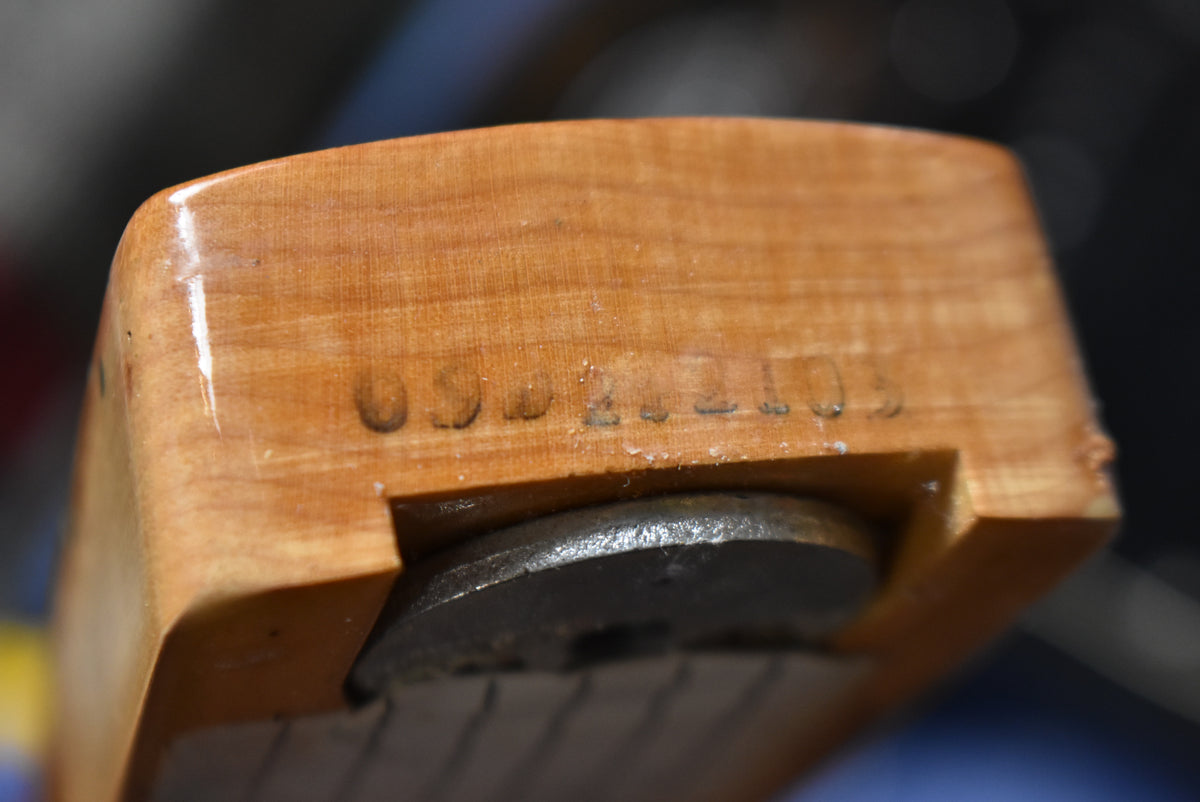 Close-up of the natural wood neck heel with a visible serial number stamped into the wood and a metal truss rod adjustment nut.