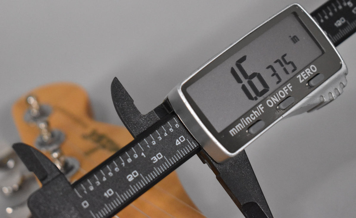 A digital caliper measures the Telecaster's light brown headstock, displaying 1.6375 inches on its screen.
