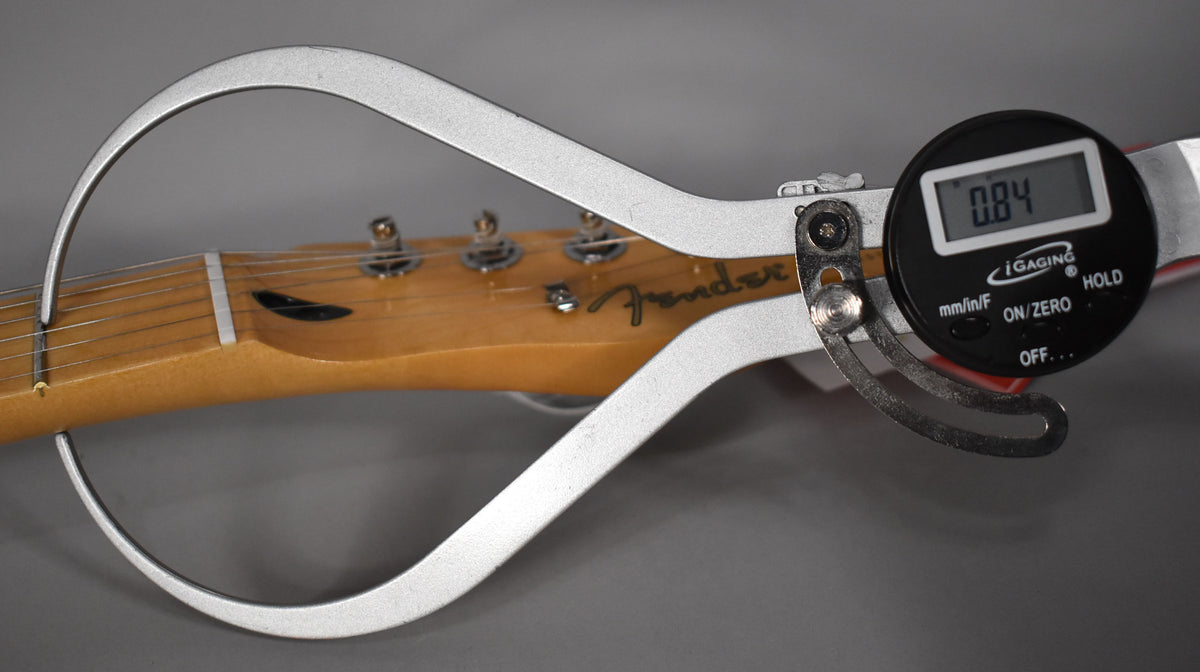 A digital caliper measures the neck thickness of a light brown maple Telecaster headstock and fretboard, displaying 0.84.