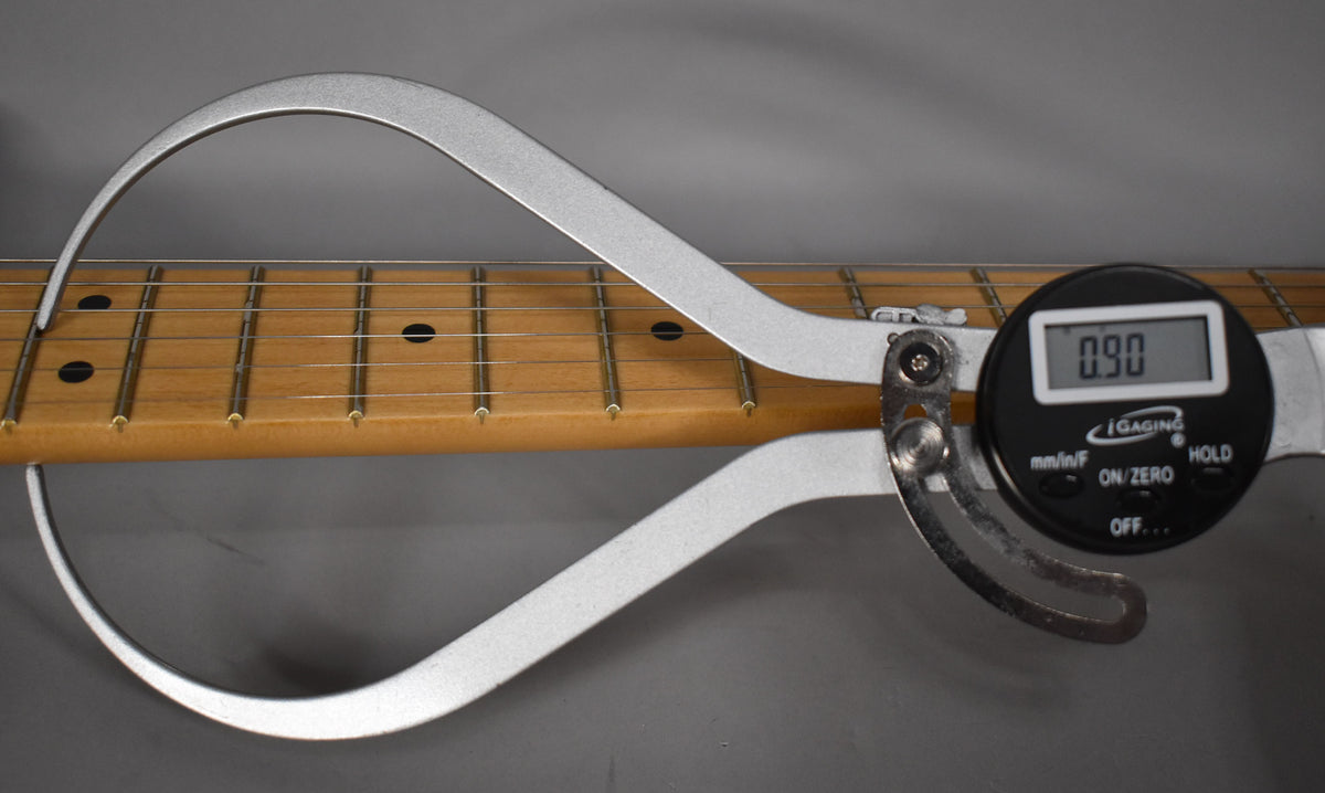 A digital caliper measures the fretboard radius of the maple neck, showing 0.90 on its display.